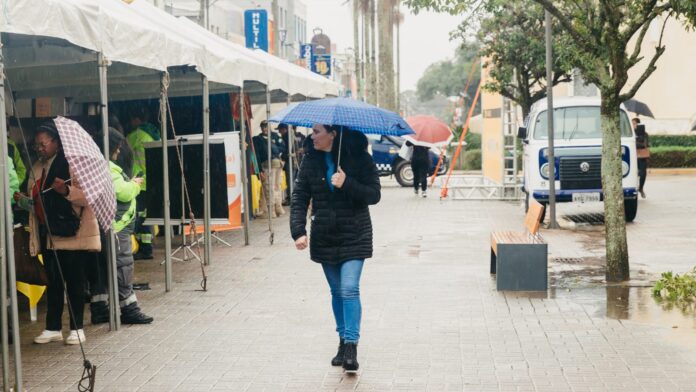 Pedestres com guarda-chuva em rua sob chuva forte no Paraná