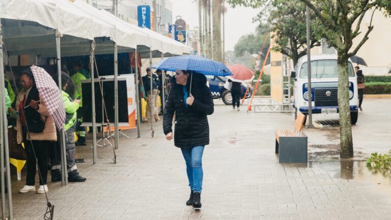 Pedestres com guarda-chuva em rua sob chuva forte no Paraná