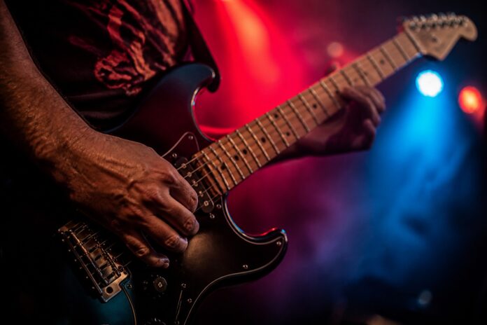Mão do guitarrista nas cordas sob luz de palco