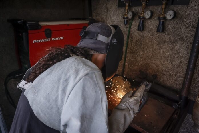 Trabalhadora solda peça metálica em oficina